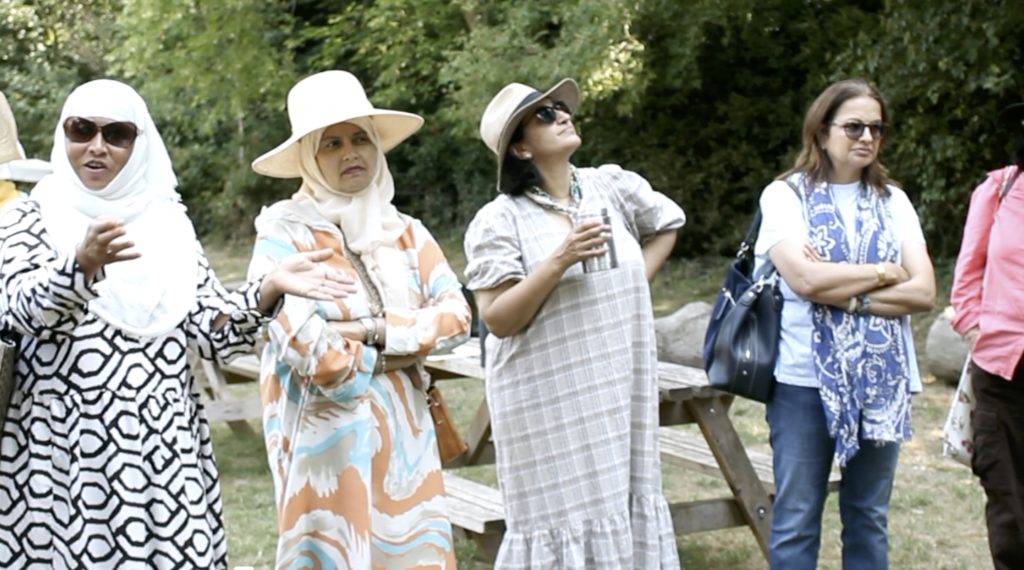 Five women dressed modestly and fashionably in an open treelaned area